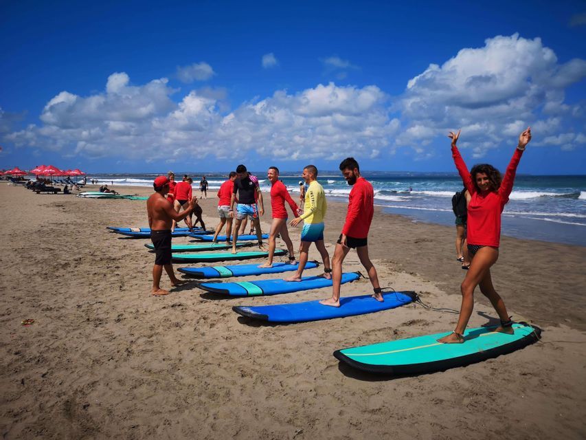 Eine WeRoad Gruppenreise mit einer Surfstunde an einem Sandstrand, wobei das Stehen auf Surfbrettern mit einem Lehrer geübt wird.