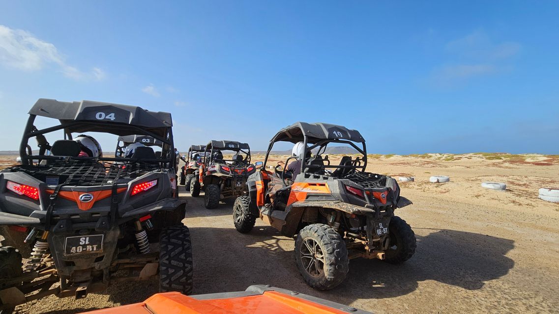Un viaggio di gruppo WeRoad con dune buggy arancioni e neri in fila su una pista sabbiosa in un paesaggio desertico.
