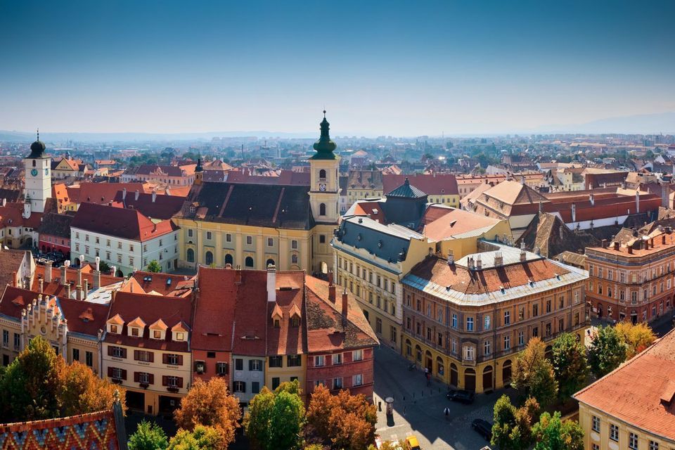 Luftaufnahme einer europäischen Stadtlandschaft mit Terrakotta-Dächern, historischen Gebäuden und einem Uhrenturm unter klarem Himmel