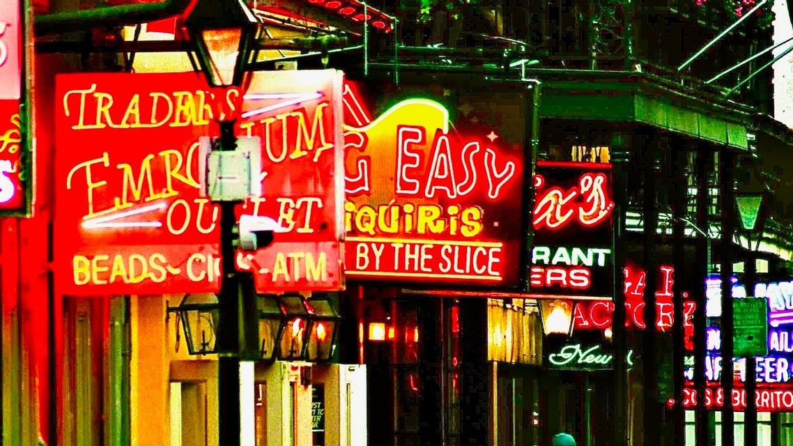 A close-up of many overlapping, colorful neon signs for bars and shops on a city street at night.