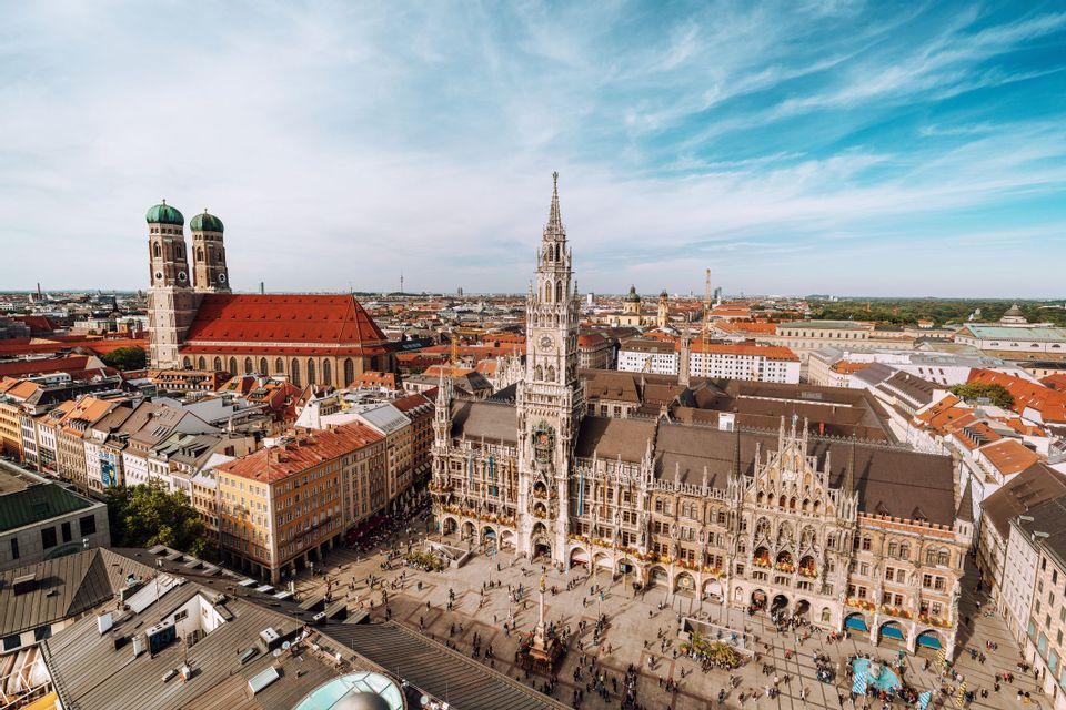 A high-angle view of a historic European city square featuring an ornate town hall and a large cathedral with twin domes.
