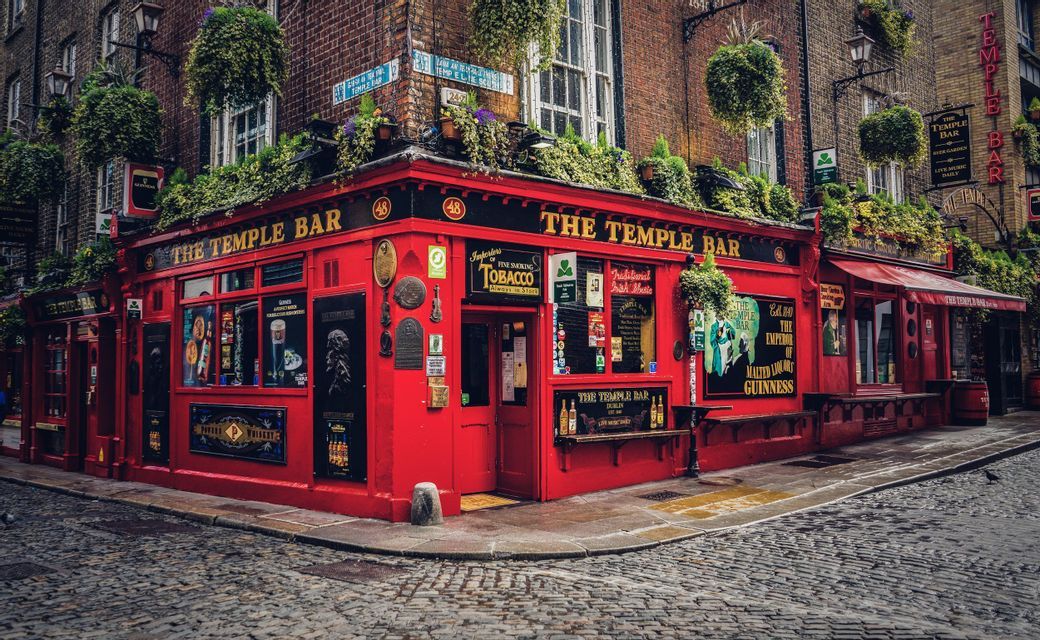 The Temple Bar pub with its bright red facade sits on the corner of a wet cobblestone street.