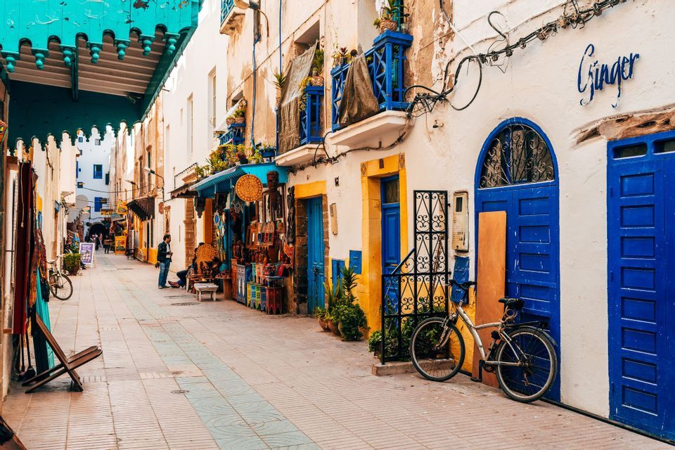 A bicycle is parked on a narrow street lined with shops and whitewashed buildings with vibrant blue doors and balconies.