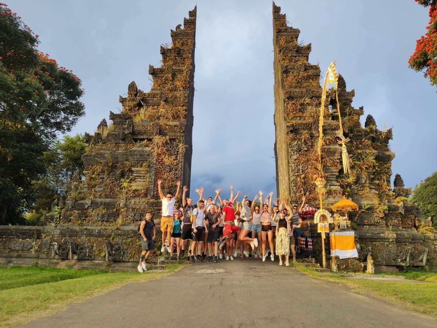 Viaje en grupo WeRoad: personas saltando y sonriendo para una foto frente a una gran puerta de piedra ornamentada, rodeada de árboles.