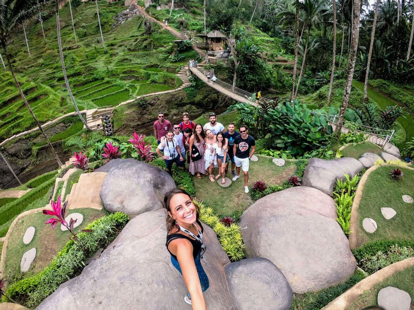 Une femme prend un selfie en plongée avec son groupe WeRoad, posant sur une colline verdoyante en terrasses parsemée de gros rochers.
