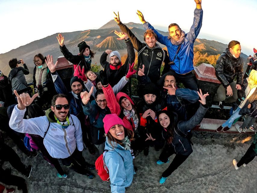 Un groupe WeRoad en voyage posant pour un selfie sur un belvédère, avec un grand volcan visible à l'arrière-plan au lever du soleil.