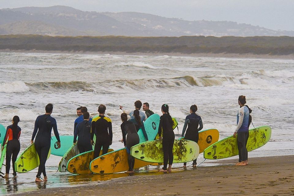 Un viaggio di gruppo WeRoad: persone in muta con tavole da surf su una spiaggia, che guardano le onde dell'oceano in attesa di una lezione di surf.