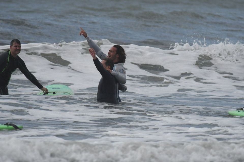 Tre uomini WeRoad in muta sorridono e festeggiano tra le onde spumose dell'oceano con le loro tavole da surf.