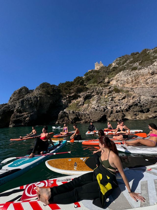 Un viaggio di gruppo WeRoad in relax su stand-up paddleboard in una baia tranquilla, con scogliere rocciose e una rovina sullo sfondo.