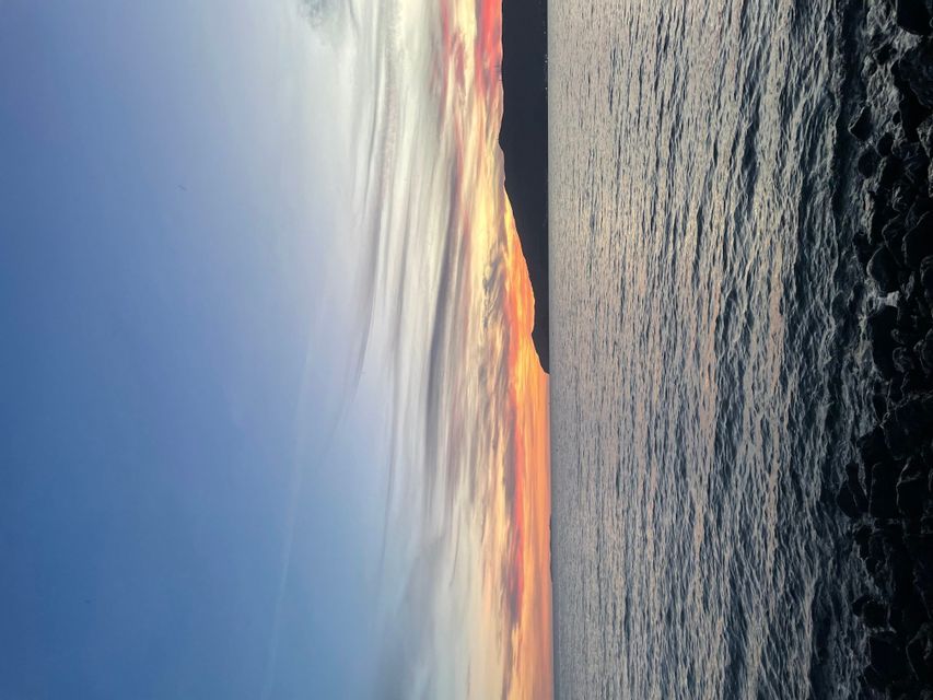 Foto verticale di un tramonto con nuvole arancioni e rosse su un mare calmo accanto a una costa rocciosa.