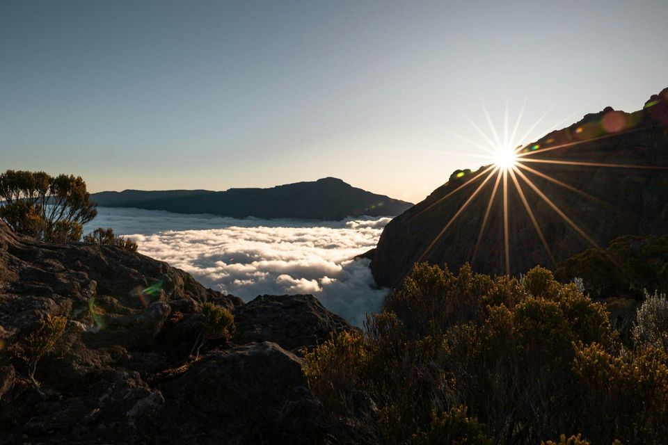 Ein Sonnenkranz erscheint, während die Sonne über einem Berggipfel aufgeht und ein Tal, gefüllt mit einem dichten Wolkenmeer, erhellt.