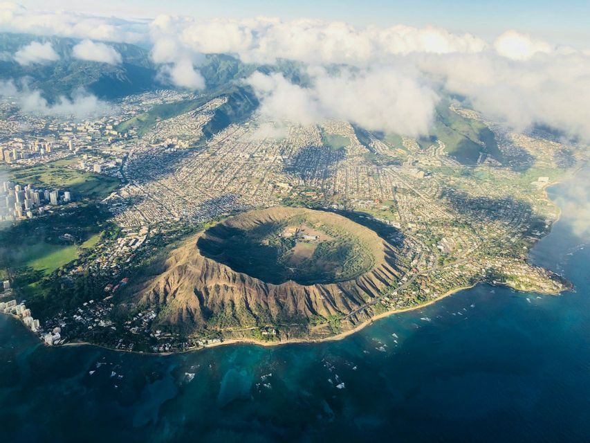 Vista aerea di un grande cratere vulcanico circolare su una costa accanto a una città popolosa e acque blu dell'oceano.
