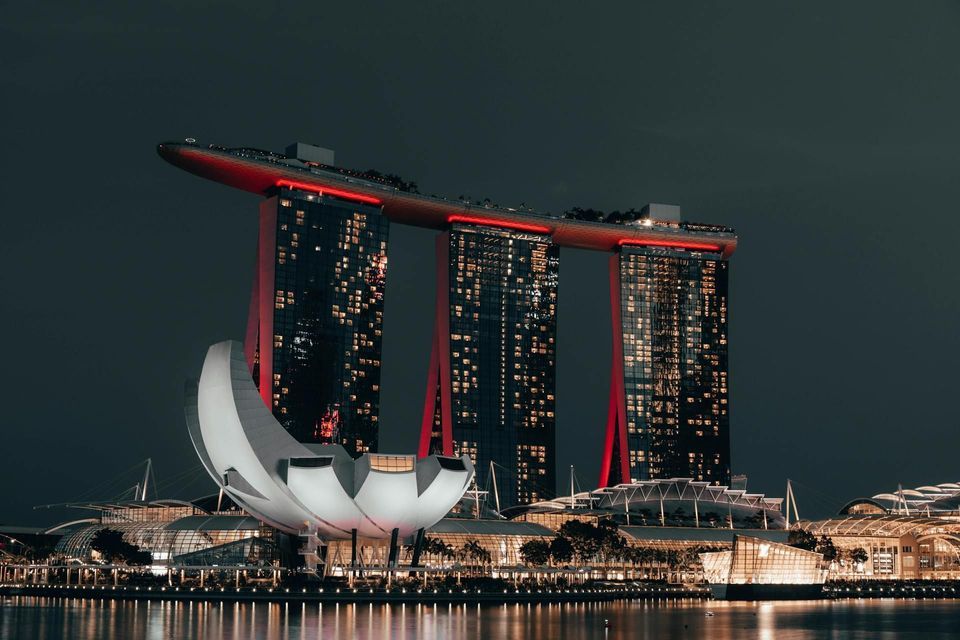 Drei beleuchtete Türme mit einer Skydeck und einem lotusförmigen Gebäude bei Nacht, mit ihren Spiegelungen auf dem Wasser.