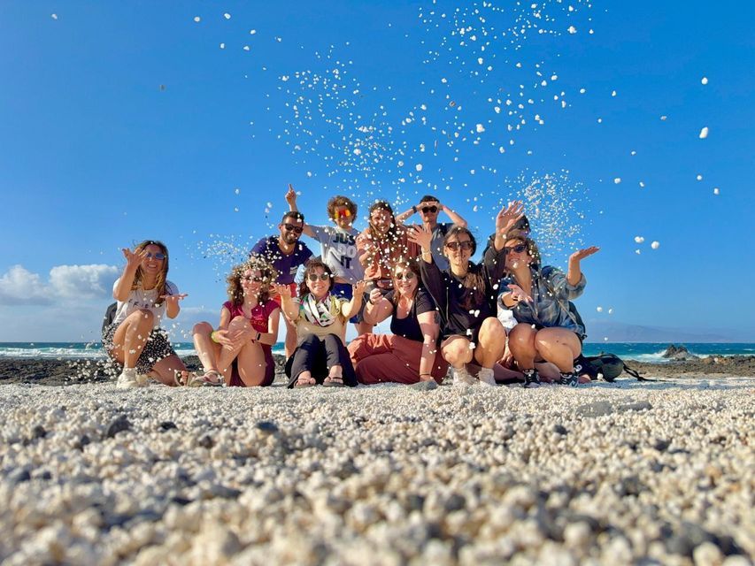 Un grupo de WeRoad lanza piedras blancas al aire mientras posa para una foto en una playa soleada.