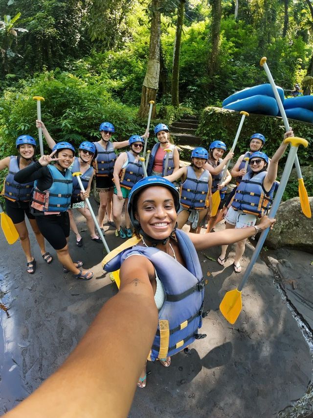 Un groupe de voyage WeRoad pose pour un selfie, portant des casques et des gilets de sauvetage et tenant des pagaies dans une forêt luxuriante.