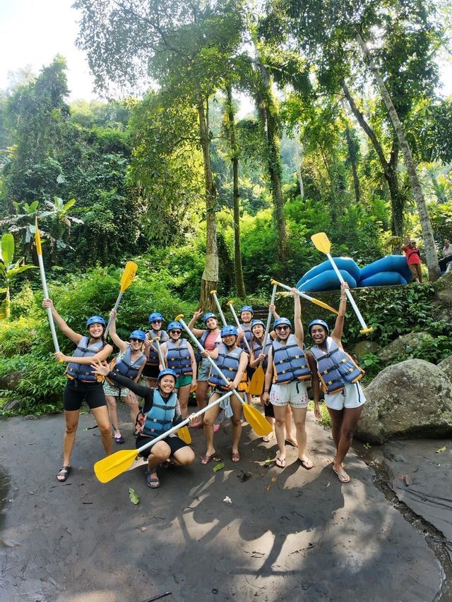 Un groupe WeRoad en gilets de sauvetage et casques posant avec des pagaies sur la rive d'une rivière dans une jungle luxuriante avant une session de rafting.