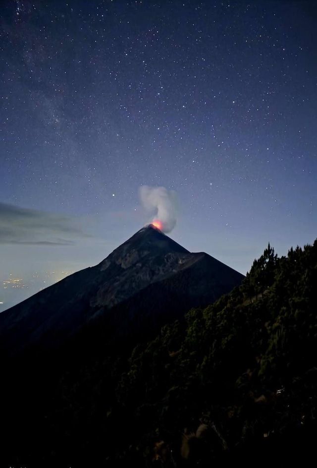 An active volcano glows with lava and emits smoke under a starry night sky.