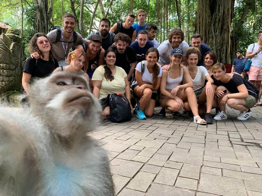Un mono se toma una selfie frente a un grupo de viaje sonriente de WeRoad posando en un patio de piedra rodeado de árboles.