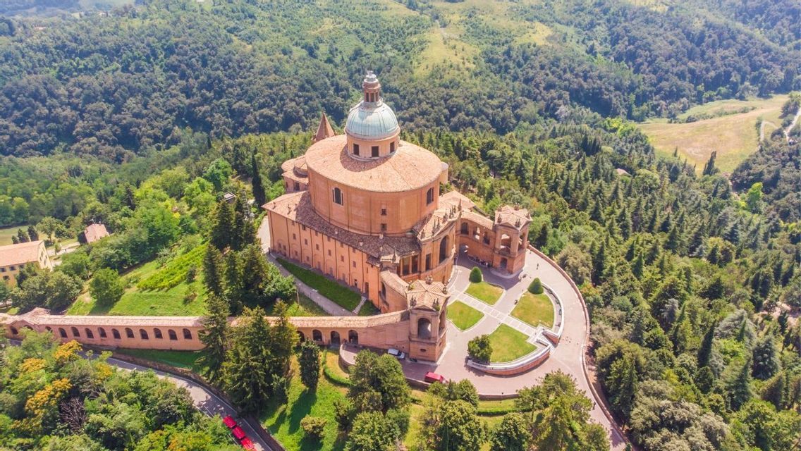Una veduta aerea di un grande santuario a cupola su una collina, circondato da una lussureggiante foresta verde e un portico ad arco.
