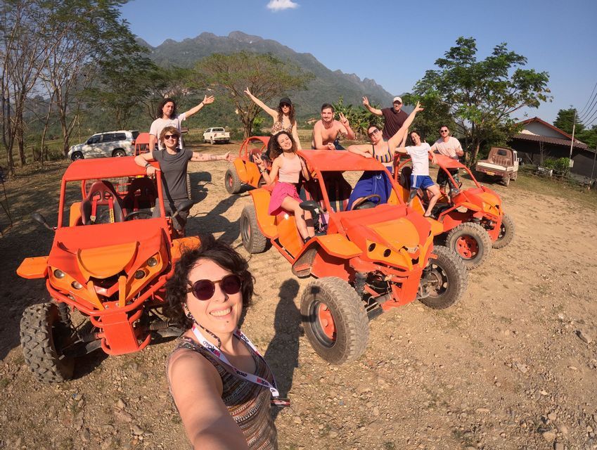 Un gruppo WeRoad che posa per un selfie con i loro dune buggy arancioni su una strada sterrata con le montagne sullo sfondo.