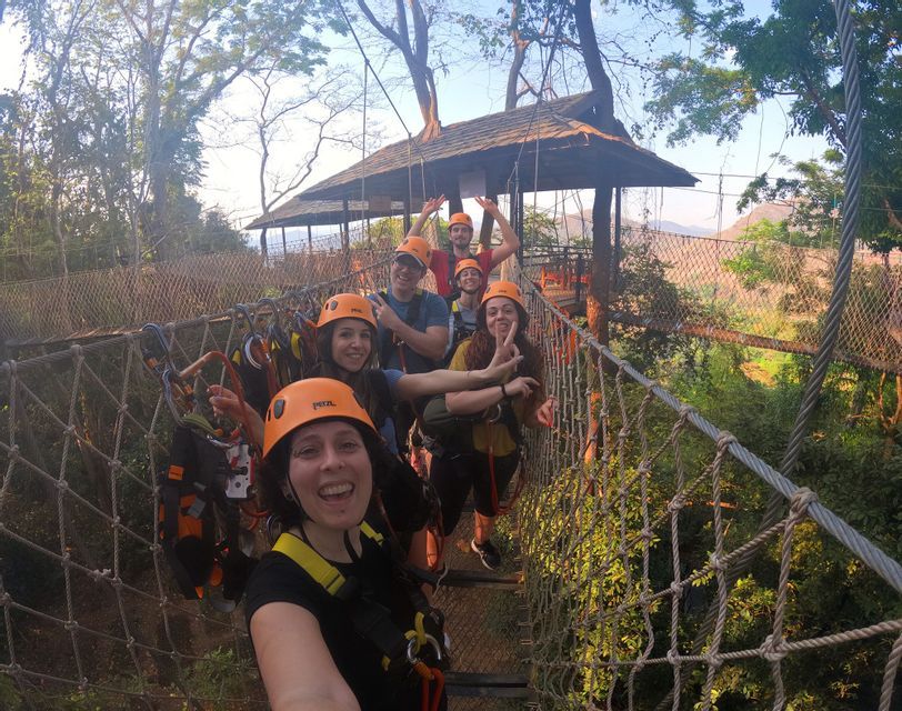 Un gruppo WeRoad con caschi e imbracature arancioni posa per un selfie su un ponte di corde sospeso, circondato dagli alberi.