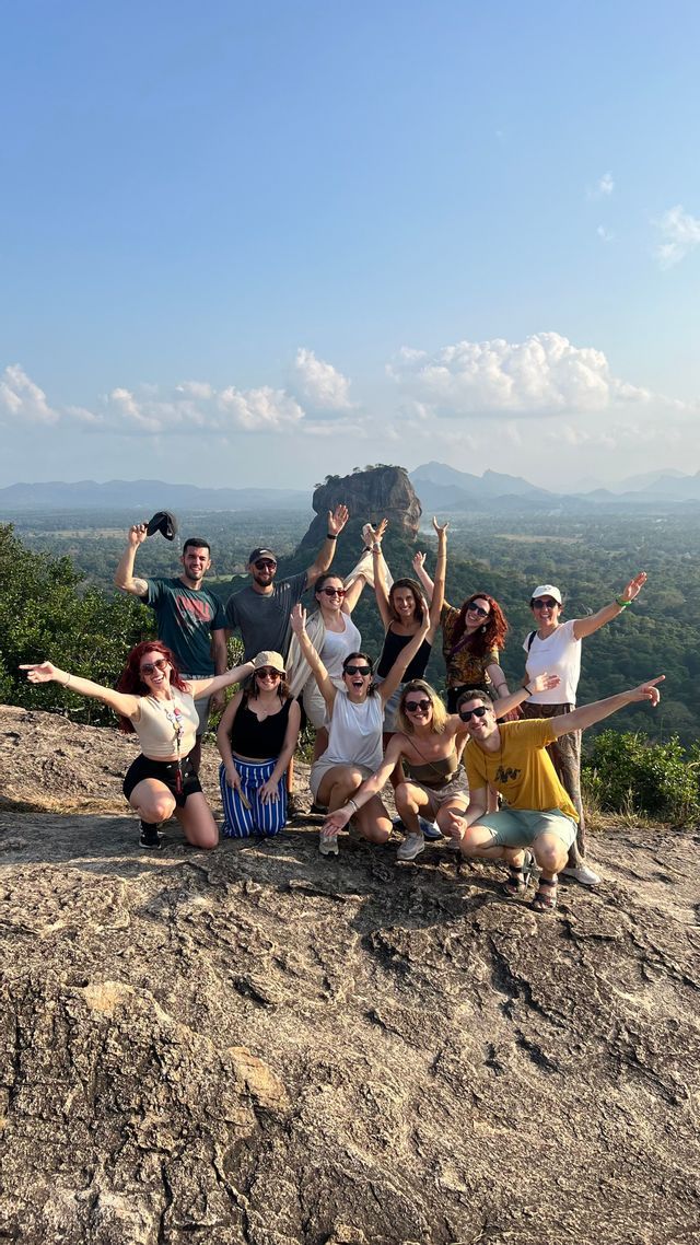 Un grupo de WeRoad posando en un mirador rocoso con un vasto paisaje verde y montañas detrás de ellos.