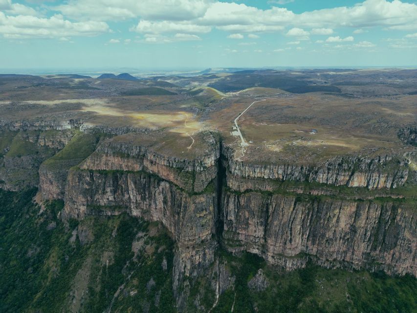 Una vista aerea di un profondo canyon che divide un vasto altopiano roccioso sotto un cielo parzialmente nuvoloso.