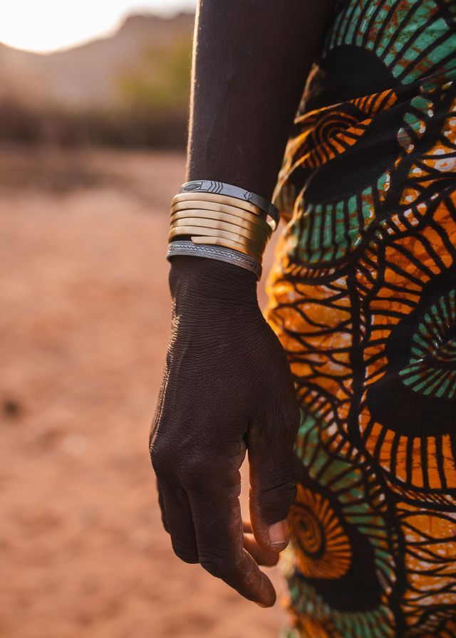 Primo piano del braccio di una persona con braccialetti d'oro e d'argento impilati, accanto a un capo d'abbigliamento a fantasia colorata.
