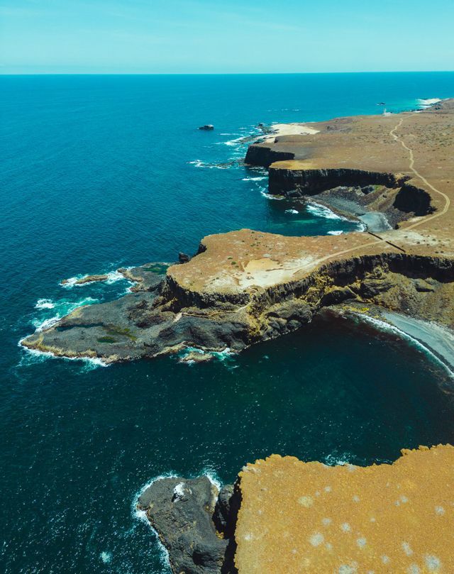Vista aerea di una costa frastagliata e rocciosa, con scogliere a picco sull'oceano blu profondo sotto un cielo limpido.