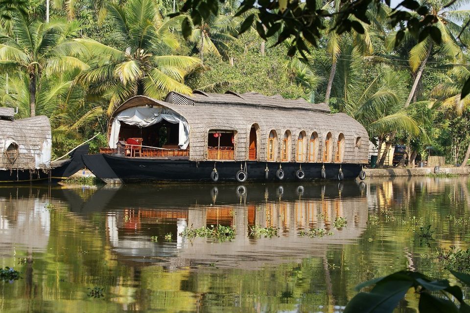 Ein traditionelles Hausboot mit Strohdach schwimmt auf stillem Wasser, umgeben von üppigen Palmen, seine Spiegelung darunter.
