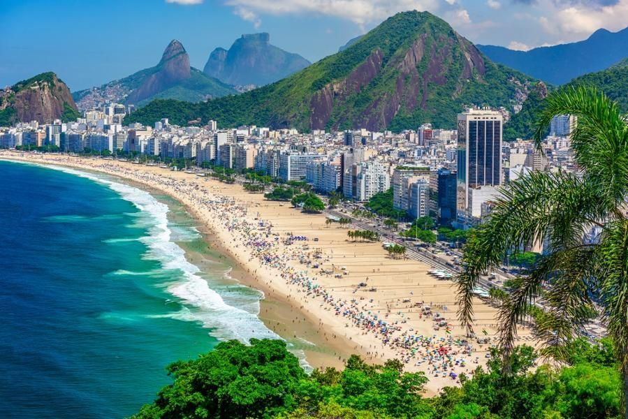 Vue plongeante d'une plage de sable bondée, longeant une ville tentaculaire au pied de montagnes verdoyantes.