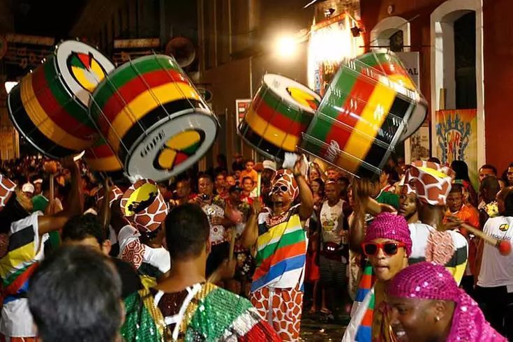 Une foule de personnes en costumes colorés célèbrent lors d'un défilé de rue la nuit, jouant de grands tambours rayés.
