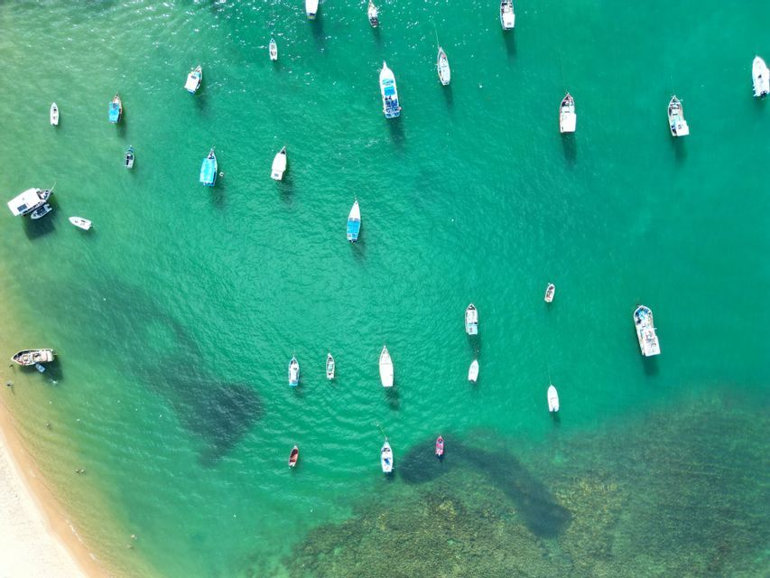 Une vue aérienne de petits bateaux flottant dans l'eau turquoise peu profonde près d'une plage de sable.