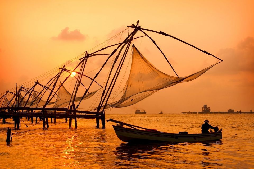 Eine Person in einem kleinen Boot treibt während eines warmen Sonnenuntergangs nahe traditioneller chinesischer Fischernetze auf dem Wasser.