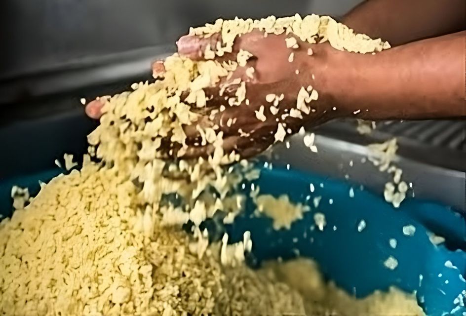 Primo piano di mani che setacciano grani di couscous, facendoli cadere in una grande ciotola blu.