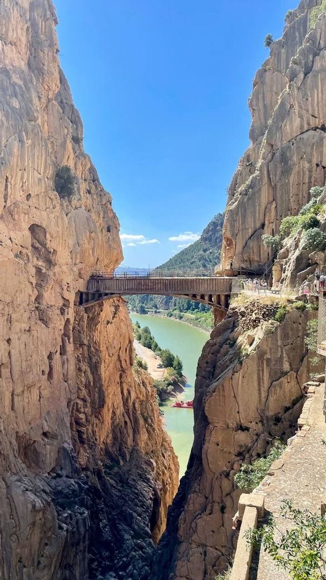 Un grupo de WeRoad cruza un puente sobre un cañón profundo con una pasarela estrecha incrustada en la roca.
