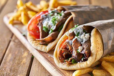 Primo piano di due gyros nel pane pita, su un tagliere di legno, serviti con patatine fritte.