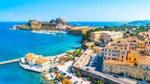 Una vista aerea di una storica città costiera con una fortezza su una penisola, circondata da un mare calmo e azzurro brillante.