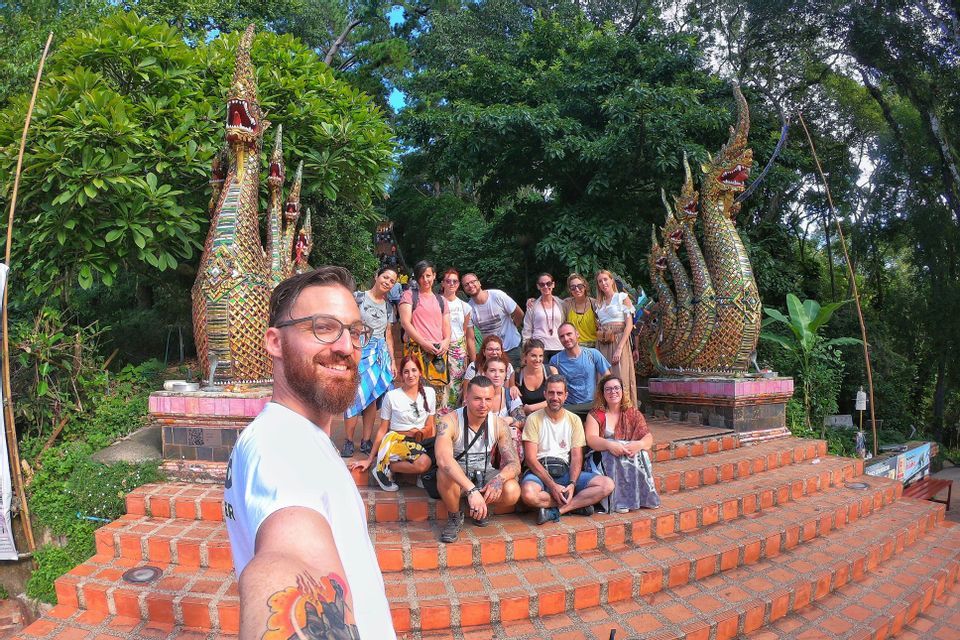 Un homme prend un selfie de son voyage de groupe WeRoad, posant sur des escaliers en briques devant deux statues de serpents ornées et à plusieurs têtes.