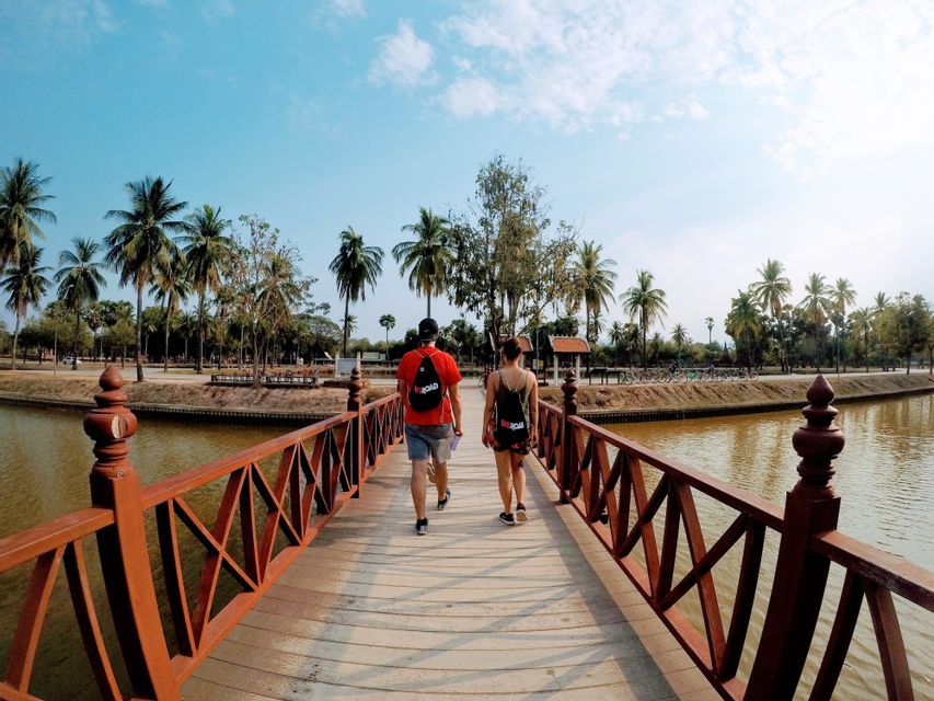 Un homme et une femme d'un voyage de groupe WeRoad, vus de dos, traversent un pont en bois au-dessus d'un canal bordé de palmiers.