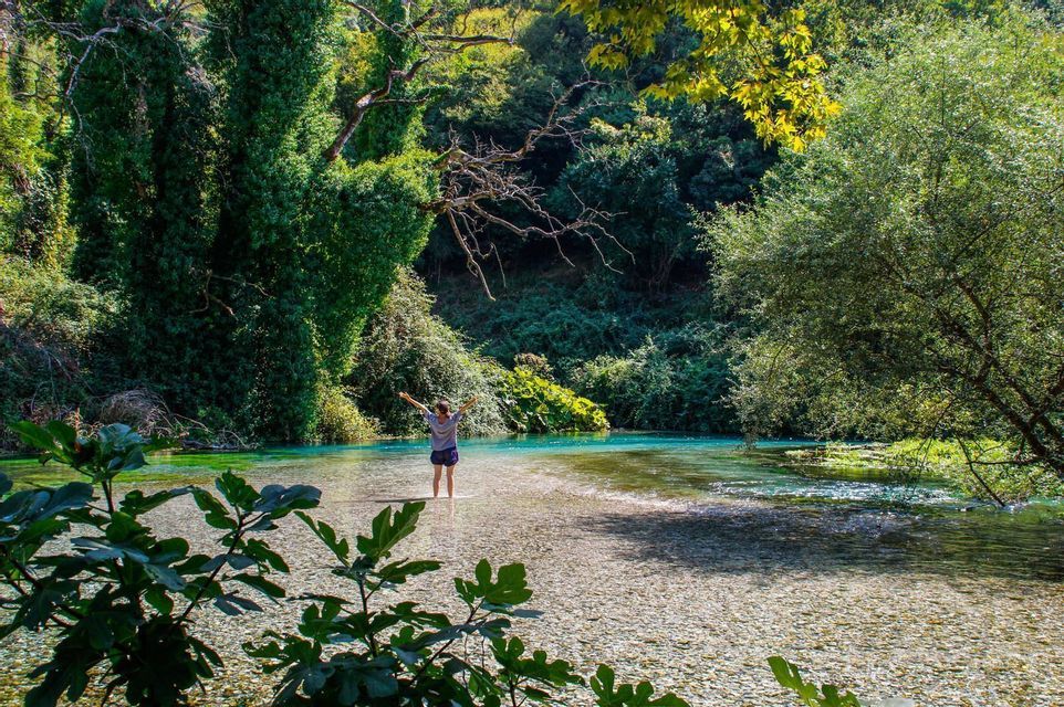 Une personne les bras tendus dans une rivière limpide, au milieu d'une forêt luxuriante.