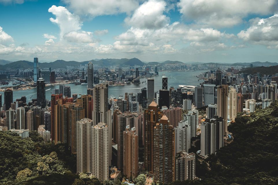 Una vista aerea di una fitta e moderna città con numerosi grattacieli che circondano una baia sotto un cielo nuvoloso.