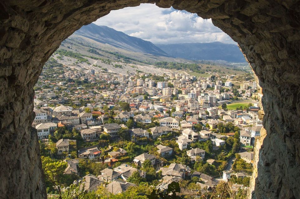 Une ville tentaculaire avec des maisons traditionnelles aux toits de pierre, vue de l'intérieur d'une arche en pierre, avec des montagnes au loin.
