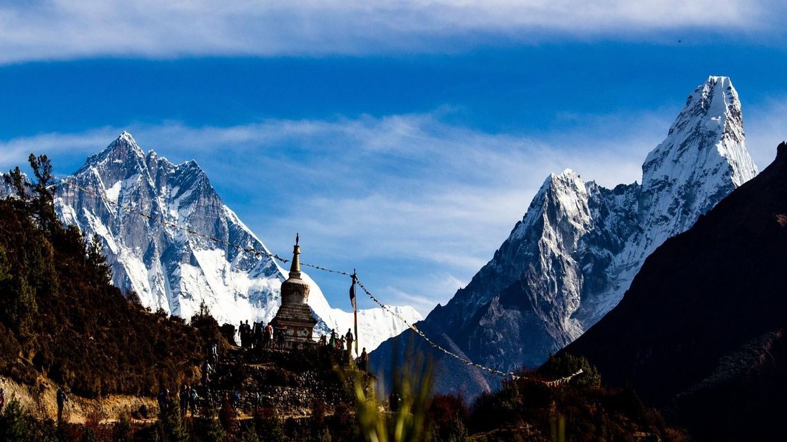 Eine WeRoad Gruppenreise steht bei einer Stupa auf einem Bergpfad, mit hohen, schneebedeckten Gipfeln vor blauem Himmel.