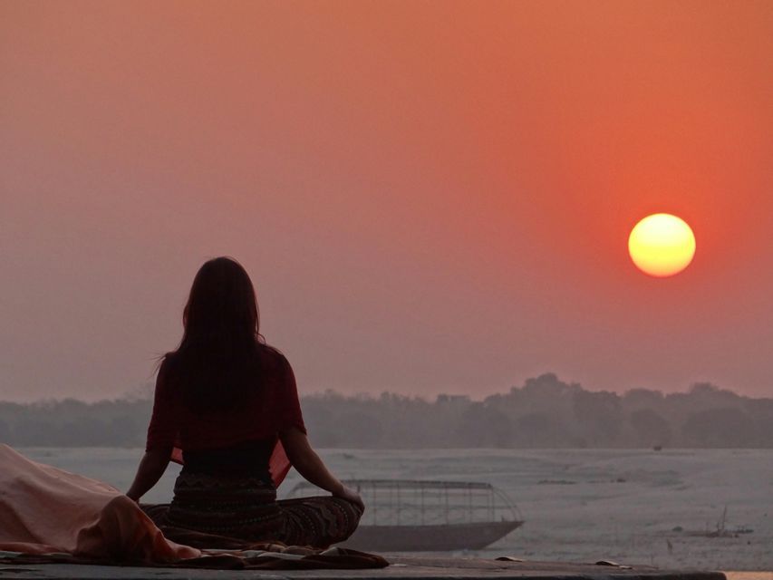 Una persona vista di spalle è seduta in posizione meditativa, mentre osserva il sole tramontare su un fiume nebbioso.