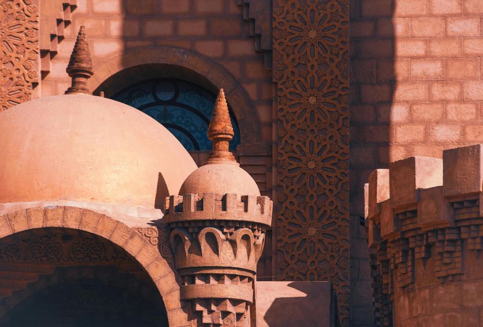 Primo piano di architettura color terracotta, ornata con cupole, minareti e intagli geometrici intricati, sotto la luce del sole.