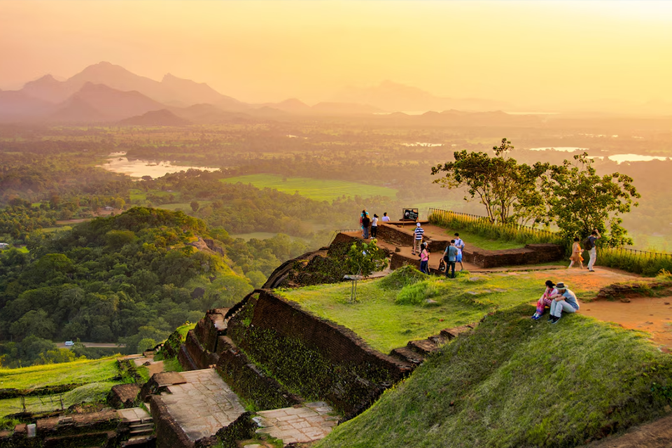 Un viaje en grupo de WeRoad se reúne en un mirador sobre ruinas antiguas, observando un atardecer sobre un valle exuberante con montañas distantes.