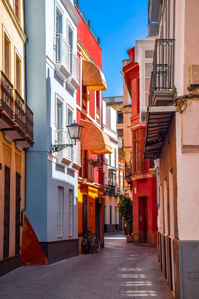 La luz del sol ilumina una calle estrecha con adoquines, bordeada por edificios coloridos en tonos rojos, azules y amarillos.