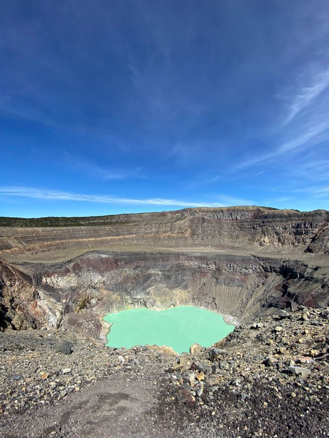Ein Blick vom Rand eines großen Vulkankraters mit einem türkisfarbenen See unter klarem blauem Himmel.