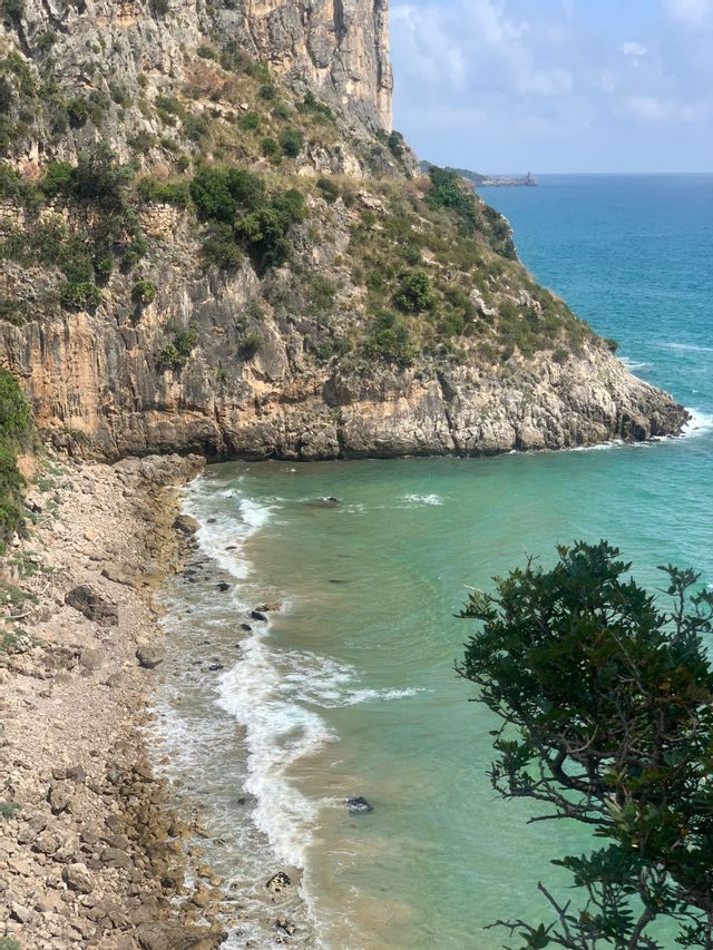 Una vista dall'alto di una scogliera rocciosa che si erge su una spiaggia di ciottoli con acqua turchese che lambisce la riva.